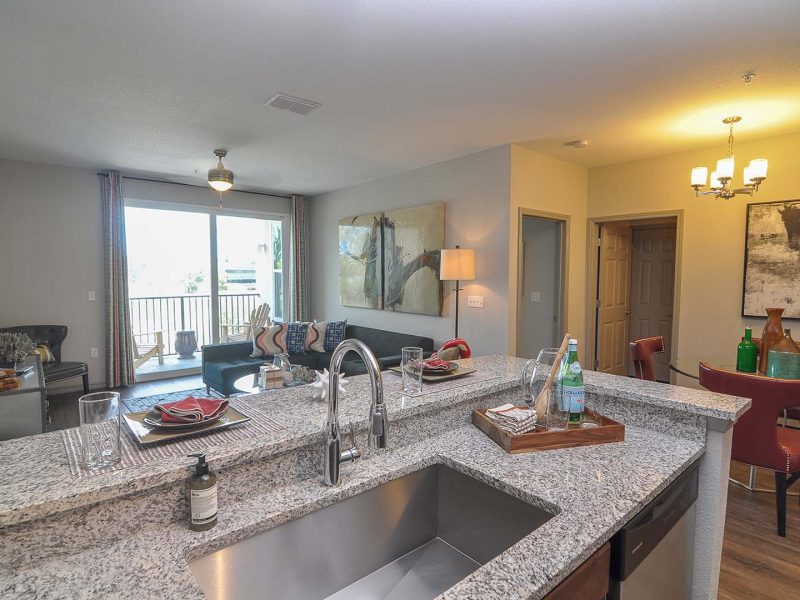 This image shows the Premium Apartment Featuring the gourmet kitchen with a breakfast bar, farmhouse sink, and stainless steel kitchen appliances. It's accessible from the dining room to the living area.
