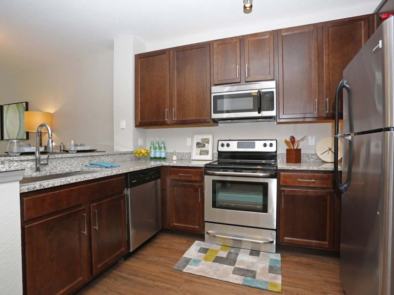 This image shows a fully equipped kitchen with stainless steel kitchen appliances, granite countertops, a breakfast bar, and a farmhouse sink.