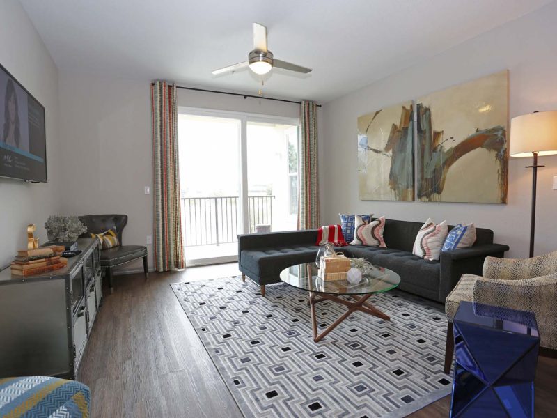 This image shows the premium feature in the living room area with modern floor mats and modern interior design that was ideal for a neat atmosphere. There's a hanging TV, ceiling fan with a trendy plank wood flooring.