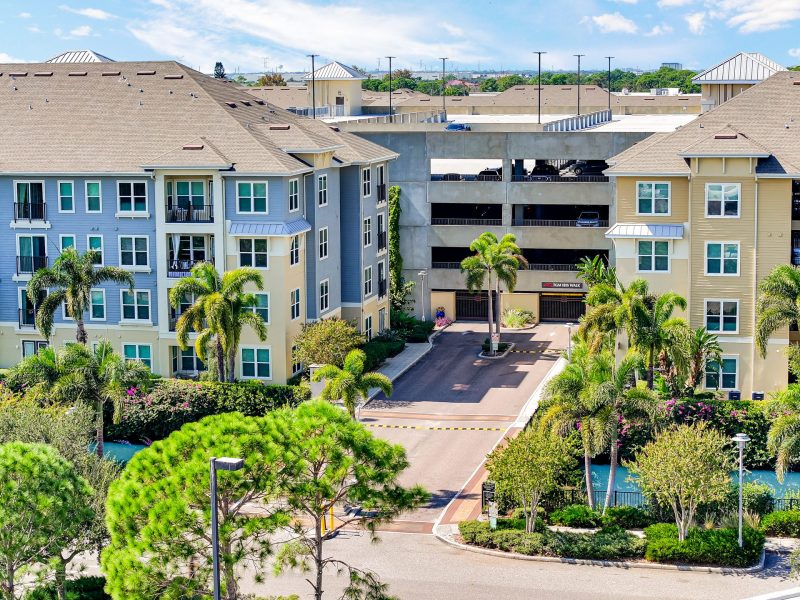 Modern coastal apartment complex with palm trees, parking garage, and landscaped gardens.