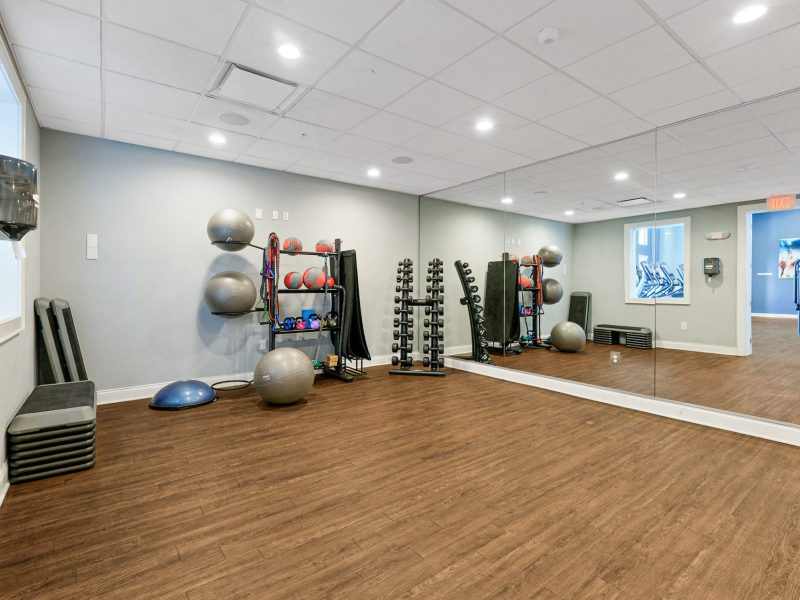 Modern fitness studio with wooden floors, exercise balls, dumbbells, and mirrors for workouts.