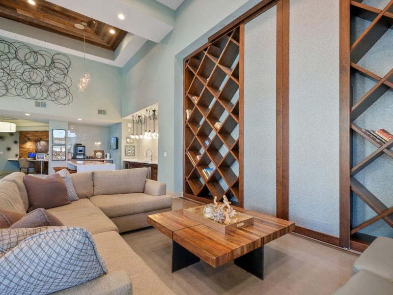 Modern living room with beige sectional sofa, blue walls, and geometric wine rack decor.