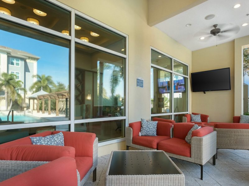 Modern poolside lounge with wicker chairs, red cushions, and large windows at TGM Ibis Walk.